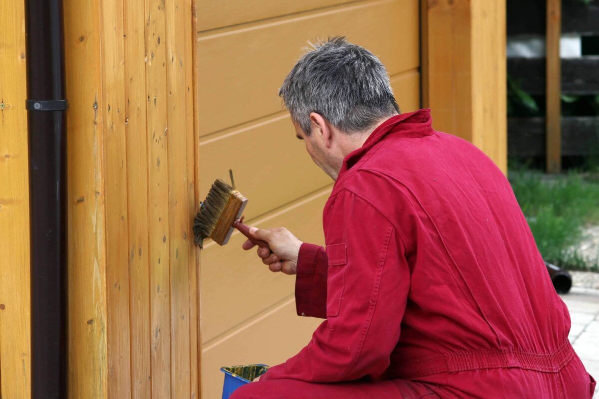 Mitarbeiter streicht einen Hundezwinger mit Holzlasur in Wunschfarbe